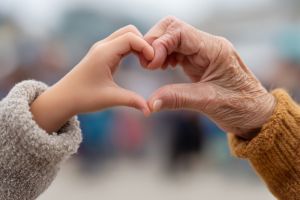 Eine junge und eine alte Hand zeigen gemeinsam ein Herz