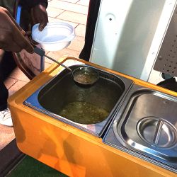 Eine Hand hält eine Kelle mit Suppe.