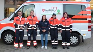 Menschen in Malteser Einsatzkleidung vor dem Malteser Herzenswunschkrankenwagen