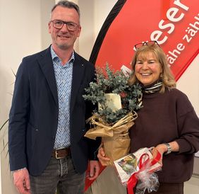 Ein Mann und eine Frau stehen vor einer Malteser Fahne, die Frau hat Geschenke in der Hand