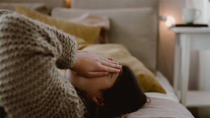 Eine junge Frau liegt mit den Händen vor ihrem Gesicht auf einem Bett.