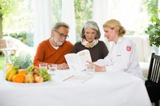Malteser Mitarbeiterin berät ein älteres Paar zu Hause.