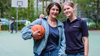 Eine junge Frau im Malteser Shirt legt einem Mädchen mit einem Basketball den Arm um die Schulter.