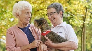 Ältere Dame streichelt einen Dackel den eine Ehrenamtliche vom Hundebesuchsdienst hält