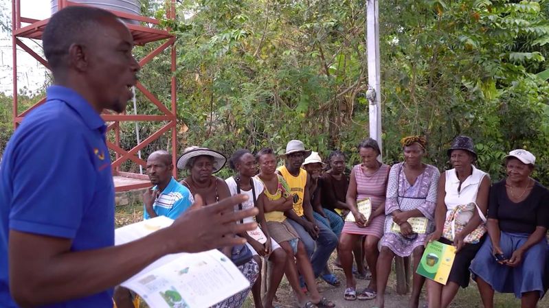 Eine Gruppe Menschen hört einem Mann mit blauem Poloshirt zu