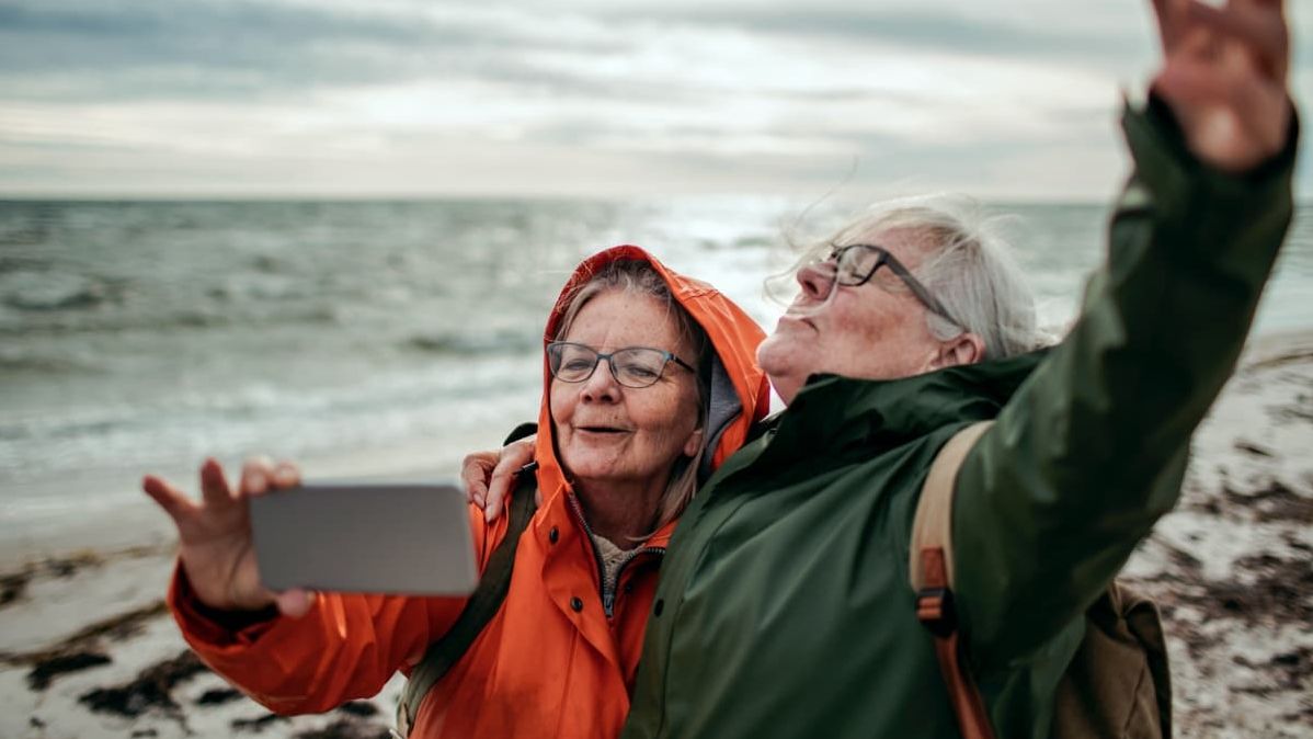 Zwei ältere Damen machen einen Strandspaziergang und fotografieren sich.