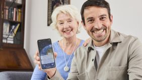 Mutter und Sohn sitzen glücklich auf einem Sofa, der Sohn hält sein Handy mit der HNR+-App in die Kamera