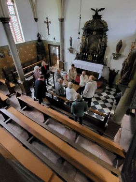 Eine Gruppe Menschen von schräg oben fotografiert in einer Kapelle mit schwarz-weißem, schachbrettartigem Boden