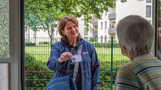 Ältere Dame öffnet die Haustür für die Mitarbeiterin der Malteser. 