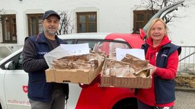 Zwei Malteser Mitarbeiter stehen mit Kisten mit Faschingskrapfen vor dem Dienstfahrzeug.