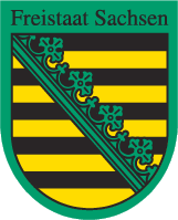 Das Bild zeigt das offizielle Wappen des Freistaates Sachsen. Im oberen Bereich steht in schwarzer Schrift der Text „Freistaat Sachsen“. Darunter befindet sich ein schildförmiges Wappen mit einer grünen Umrandung. Innerhalb des Wappens sind mehrere waagerechte schwarze und goldgelbe Streifen zu sehen, die sich abwechseln. Diagonal von links oben nach rechts unten verläuft ein grüner Streifen (bekannt als Rautenkranz), der mit stilisierten, kleeblattartigen Ornamenten verziert ist.