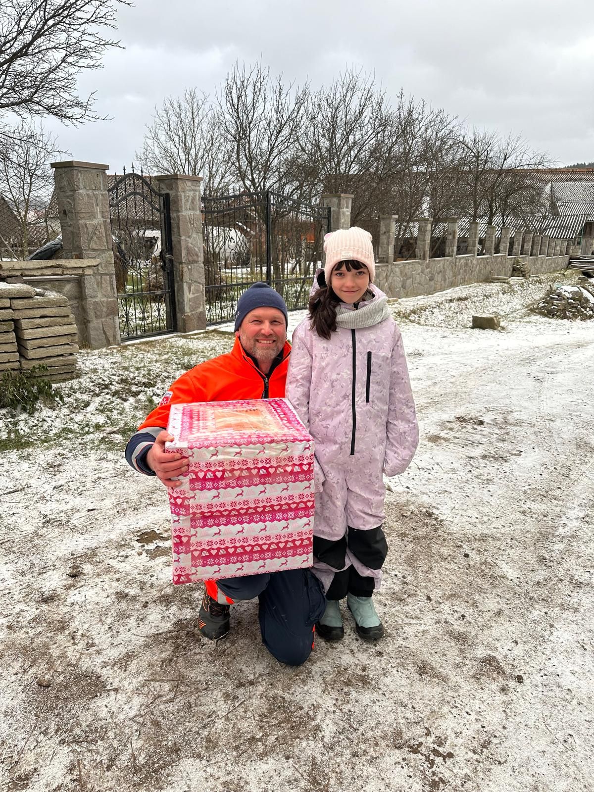 Mann in Malteser Kleidung und Kind mit Weihnachtspaket in verschneiter Landschaft