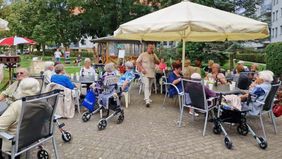 Ältere Menschen sitzen in einem Innenhof an Tischen.