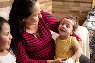 Eine Frau hält ein krankes Kind in ihrem Arm. Sie lachen gemeinsam.