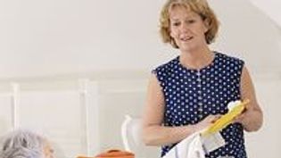 Eine Frau spült ab und unterhält sich mit einer älteren Frau im Rollstuhl.