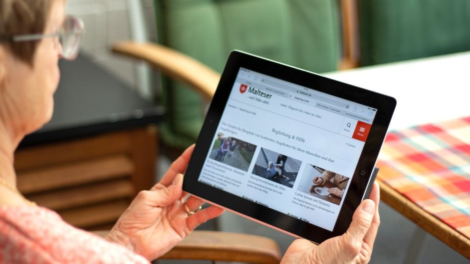 Eine ältere Frau hält ein Tablet in der Hand, auf der Artikel zum Thema „Begleitung & Pflege“ des Malteser Magazins „dabei.“ abgebildet sind.