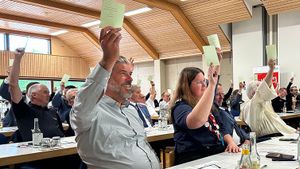 Frauen und Männer der Malteser sitzen an Tagungstischen zeigen Karten in die Höhe