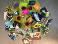 Verschiedene Fotos, Rosen, Kerzen und Erinnerungsgegenstände liegen kreisförmig auf einem grünen Tuch am Boden ausgelegt. Die Bilder zeigen unter anderem Naturmotive, persönliche Erinnerungen, Trauerszenen und Symbole rund um Leben, Abschied und Gedenken.
