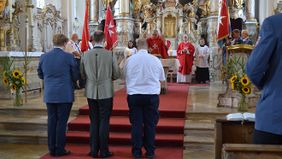 Domkapitular Platschek hebt die Hände zum Segen, von hinten drei neu berufene ehrenamtliche Führungskräfte, um den Altar herum Fahnenabordnungen