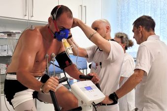 Leistungstest auf dem Ergometer mit Atemmaske, betreut von drei medizinischen Fachkräften in weißer Kleidung.