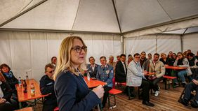 Eine Frau spricht in einem Zelt vor sitzenden Zuhörern an Tischen.