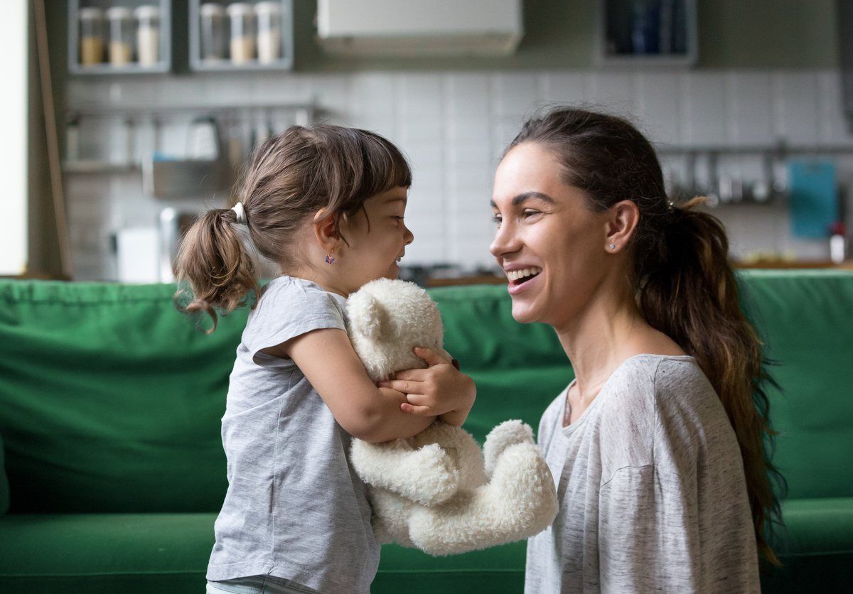 Eine lächelnde Frau mit einem Mädchen, das ein Kuscheltier im Arm hält