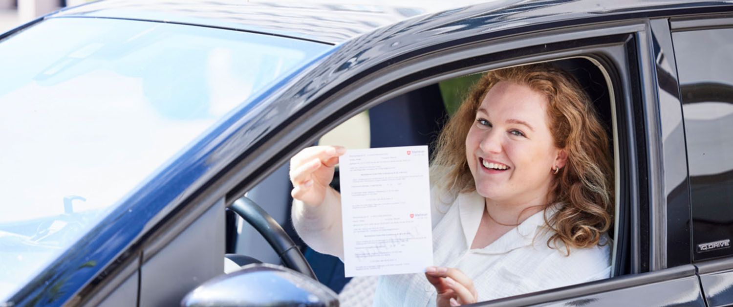 Eine Frau sitzt im Auto und hält den Erste-Hilfe-Nachweis für den Führerschein in den Händen.