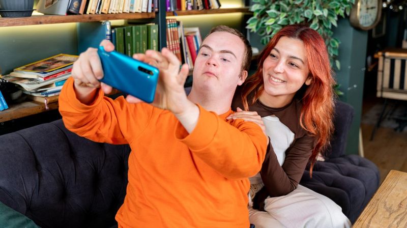Junger Mann und lächelnde junge Frau machen ein Selfie auf einem Sofa 