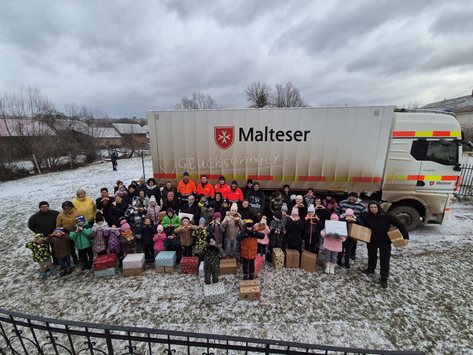 Menschen mit Paketen stehen vor einem Malteser Lkw