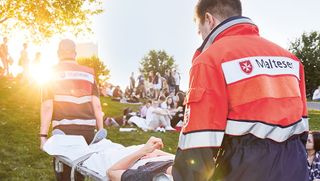 Malteser Einsatzsanitäter tragen einen Verletzten über ein Festivalgelände.