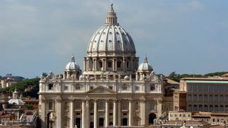 Der Petersdom in Rom mit Sicht auf Säulen und Kuppel vor blauem Himmel.