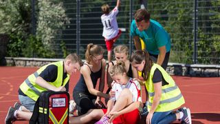 Malteser Schulsanitäter versorgen ein Mädchen, das sich beim Sport verletzt hat.