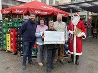Vier Personen mit Nikolaus stehen vor einem Getränkemarkt und hält einen Spendenscheck hoch.