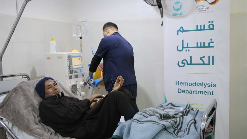 Ein Mann auf einem Krankenbett, dahinter ein weiterer Mann, der eine Dialysemaschine bedient. 