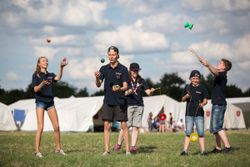 Auf dem Foto zu sehen sind mehrere Kinder und Jugendliche in Malteser Jugend Shirts beim Jonglieren auf einer Wiese vor mehreren Zelten.