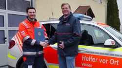 Zwei Männer vor einem Malteser Einsatzfahrzeug reichen sich die Hand.