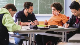 Malteser Schulbegleiter sitzt mit Schülern im Klassenzimmer.