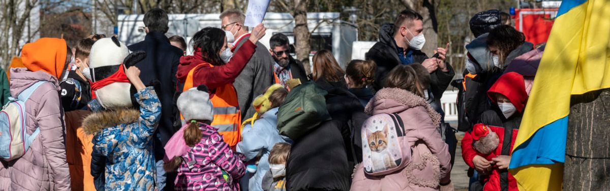 Geflüchtete ukrainische Kinder; auf der rechten Seite eine ukrainische Flagge an einem Baum.