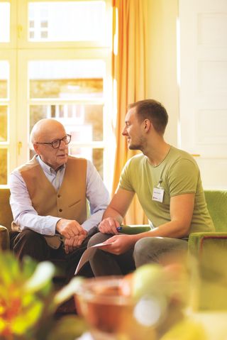 Man mit Malteser Namensschild sitzt neben älteren Herrn