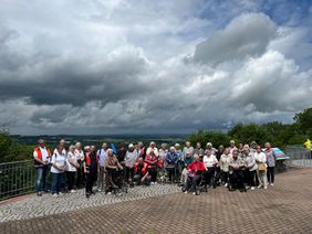 Viele Senioren stehen im Freien nebeneinander. Im Hintergrund ist es sehr bewölkt.