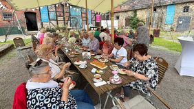 Viele Seniorinnen und Senioren sitzen an einem langen Tisch. Der Tisch ist mit Kaffee und Kuchen gedeckt.