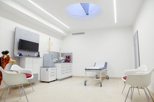 Untersuchungsraum mit Behandlungsliege, Skelettmodellen und mehreren Stühlen.