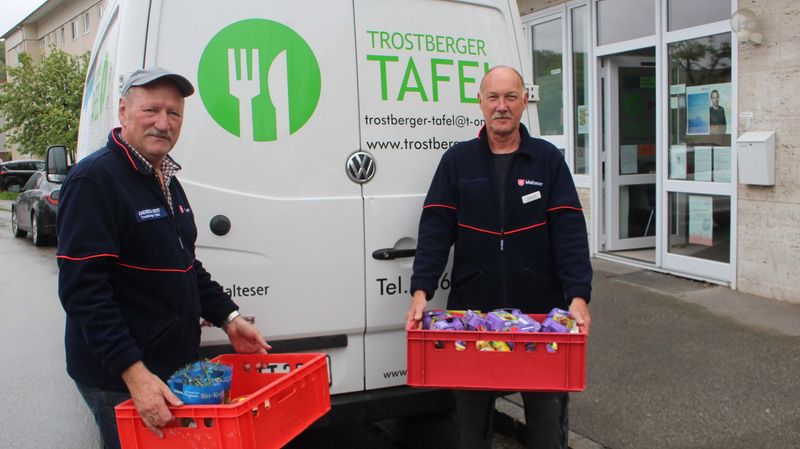 Zwei Männer mit roten Lebensmittelkisten vor einem Lieferwagen der Trostberger Tafel