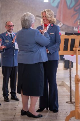 Eine Frau steckt einer anderen bei einer Zeremonie ein Abzeichen an die Uniform.