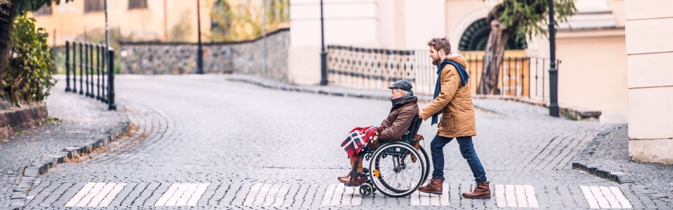 Mann schiebt Senior im Rollstuhl