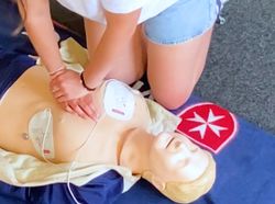 Eine Erste-Hilfe-Puppe liegt auf dem Boden. Eine Person übt die Lebensrettung.