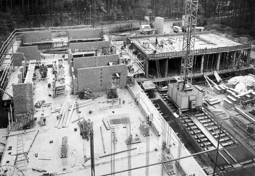 Baustelle eines Gebäudes mit Mauerwerk, Kran und arbeitenden Personen.