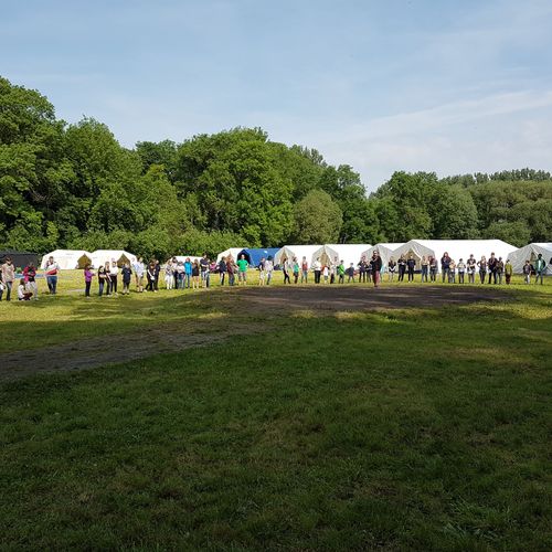Auf einer Wiese stehen im Hintergrund mehrere Zelte.