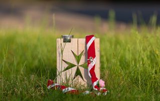 Malteser Kreuz aus Holz steht in der Wiese und auf ihm liegt ein Malteser Jugend Tuch