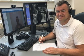Arzt mit Headset führt eine Videosprechstunde am Computer durch und sieht MRT-Bilder auf dem Monitor.